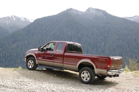 2006 Ford F-250 - A maroon Ford Super Duty pickup truck is parked on a gravelly surface with a forested mountain range behind it.
