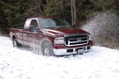 2006 Ford F-250 - A maroon Ford F-250 truck navigates a snowy path, spraying snow as it moves.