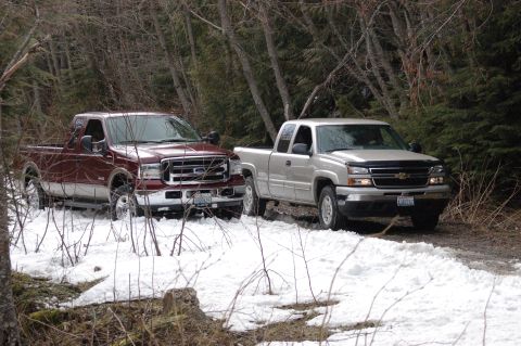 2006 Ford F-250 - Two pickup trucks, a maroon Ford F-250 and a silver Chevrolet Silverado, navigate a snowy, wooded trail.