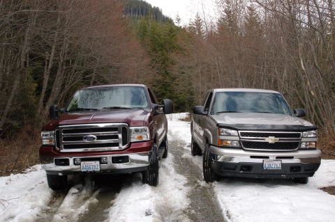 2006 Ford F-250 - Two pickup trucks are parked on a snow-covered road, surrounded by bare trees and evergreens.