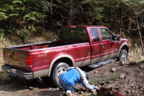 2006 Ford F-250 - A person works on the rear tire of a red 2006 Ford F-250 pickup truck off-road.