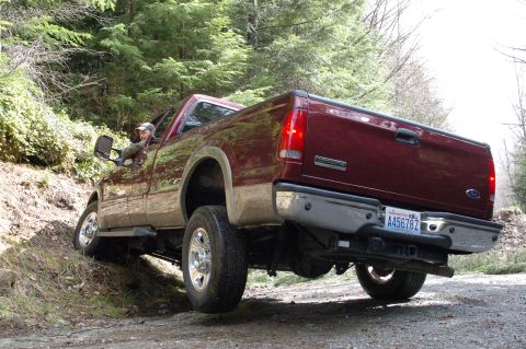 2006 Ford F-250 - A maroon Ford F-250 Super Duty pickup truck navigates a dirt road with trees in the background.