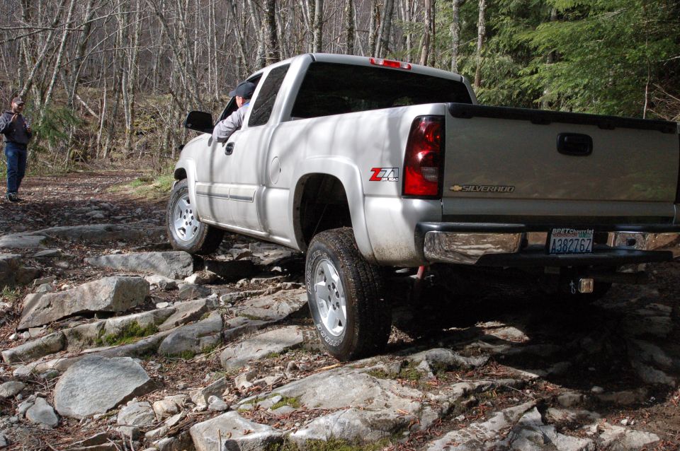 Silver Chevrolet Silverado pickup truck with Z71 badging driving on a rocky forest trail. License plate A382762