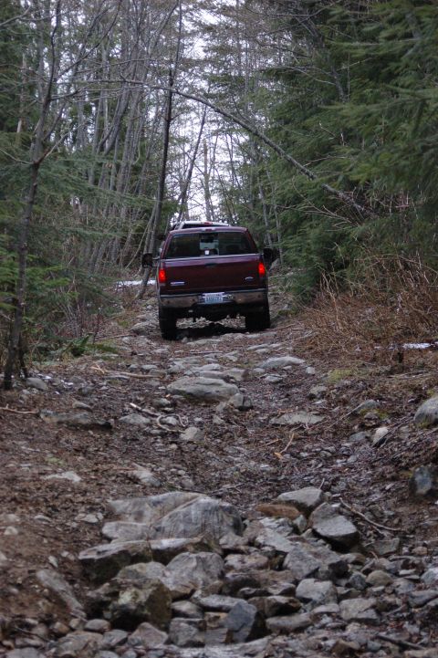 2006 Ford F-250 - Ford F-250 navigates a challenging, rocky trail in a wooded area.