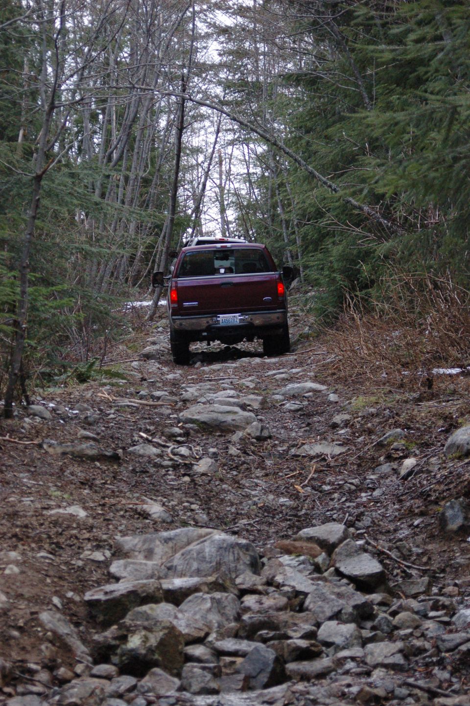 2006 Ford F-250 driving on a rough, rocky path through a dense forest