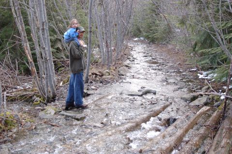 2006 Ford F-250 - A man carries a child on his shoulders while walking along a stream-filled path in a wooded area.