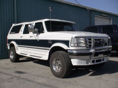 1993 Ford C-350 (Centurion Conversions) - This modified Ford van, likely a 1992 model, is parked in front of a blue building next to a dark pickup truck.