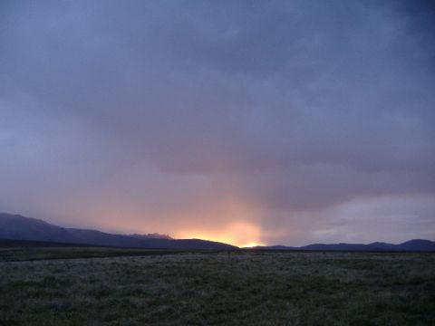 1979 Ford Bronco - A vast open field stretches towards distant mountains under a dramatic, cloudy sunset sky.