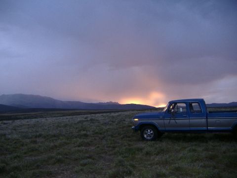 1979 Ford Bronco - Pickup truck sits in a field as the sun sets behind distant mountains.