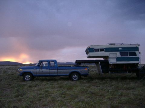 1979 Ford Bronco - A Ford pickup truck tows a camper across a grassy field during sunset.