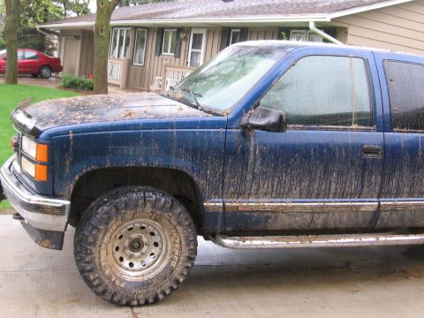 1995 GMC Sierra 1500 - A muddy blue 1995 GMC Sierra 1500 pickup truck is parked in front of a house on a rainy day.