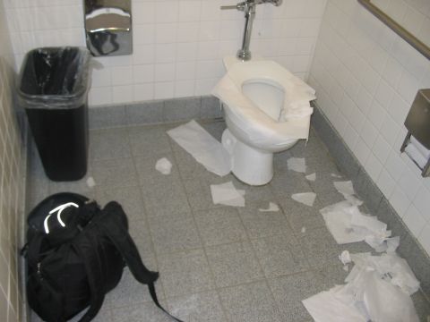 1991 Ford Bronco - A messy toilet stall with toilet paper scattered on the floor and a black backpack on the ground.