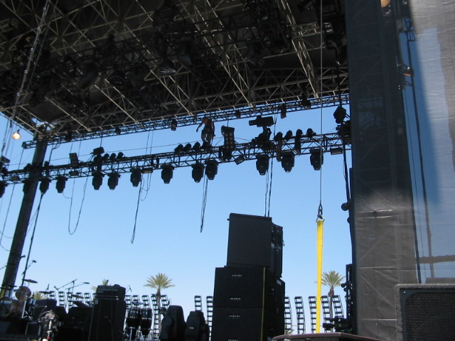 Stage lighting rig with speakers and palm trees under a clear blue sky
