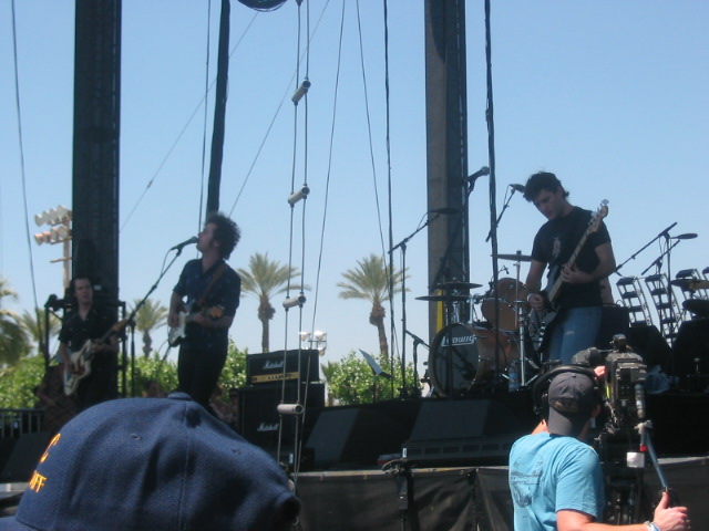 Band performing on an outdoor stage with palm trees in the background