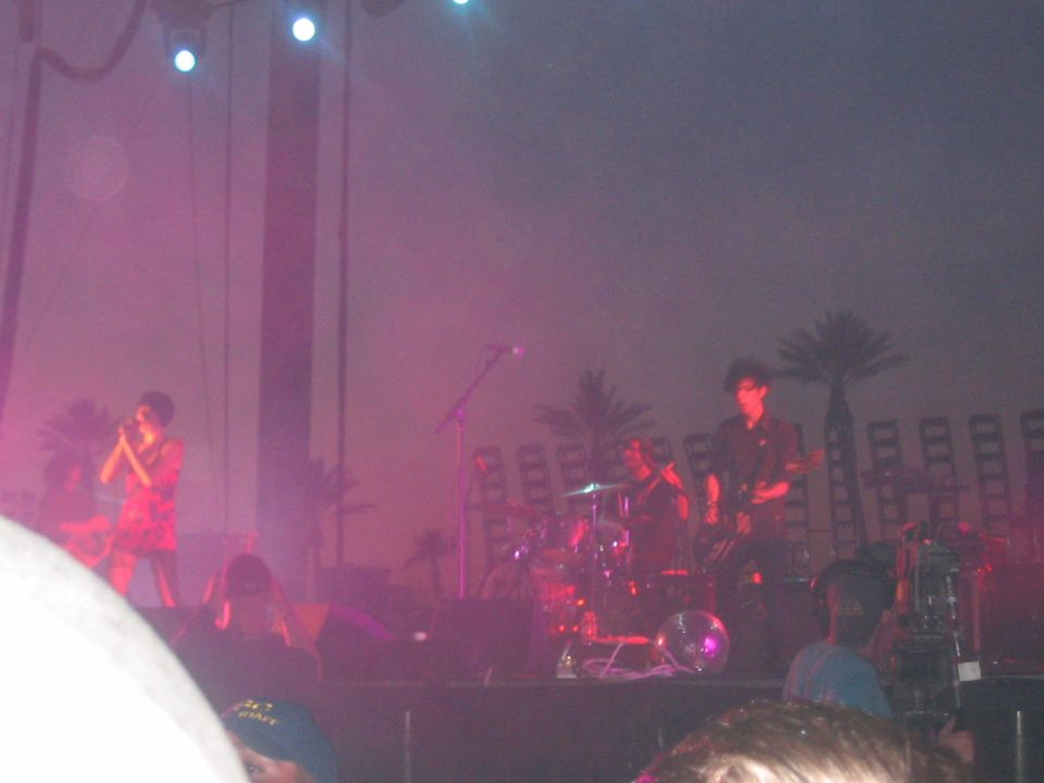 Band performing live on stage with palm trees and stadium seating in the background