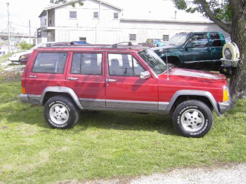 1991 Jeep Cherokee - Side view of a red 1991 Jeep Cherokee parked on a grassy area next to a building.