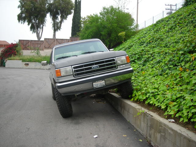 Gray Ford Bronco flexing suspension with front tire up on a curb, chrome grille and knobby tires