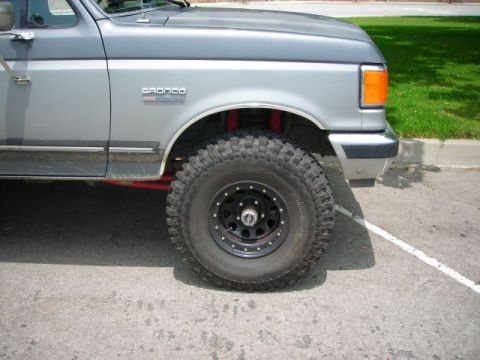1988 Ford Bronco - A two-tone grey Ford Bronco is shown from the front quarter angle, equipped with large off-road tires.