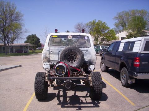 1978 Ford Bronco - A heavily modified vehicle with its rear end exposed sits in a parking lot next to a pickup truck.