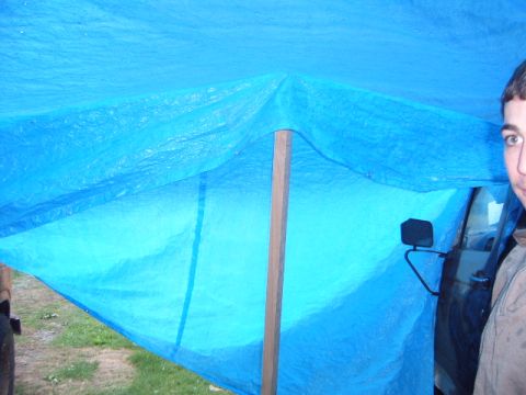 1988 Ford Bronco - A person's face and a vehicle door are partially visible beneath a blue tarp, obscuring most of the vehicle.