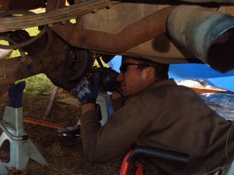 1988 Ford Bronco - A mechanic uses a grinder on the underside of a vehicle, which is supported by jack stands.