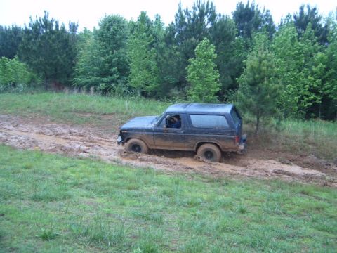 1988 Ford Bronco - Ford Bronco navigating a muddy trail with trees and grass surrounding it.