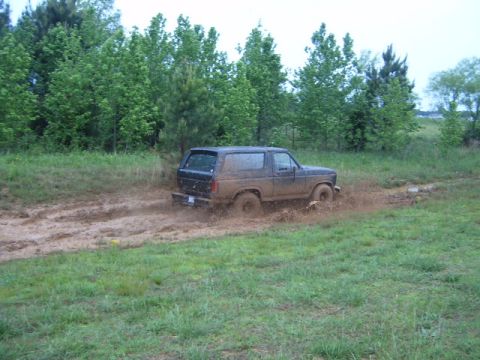 1988 Ford Bronco - A dark-colored Ford Bronco navigates through a muddy terrain, kicking up dirt and water.