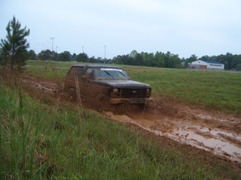 1988 Ford Bronco - Ford Bronco navigating a challenging muddy terrain with grass and trees in the background.