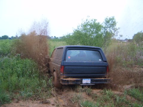 1988 Ford Bronco - This SUV is navigating a muddy trail, kicking up a large spray of dirt and water.