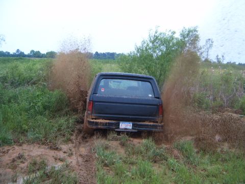 1988 Ford Bronco - A black 1988 Ford Bronco kicks up a large spray of mud as it navigates through a muddy field.