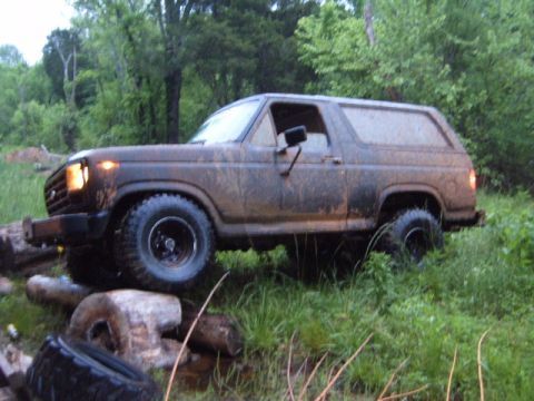 1988 Ford Bronco - Ford Bronco navigating an off-road obstacle course with muddy tires and body.
