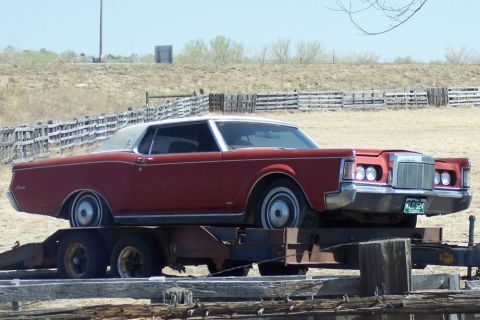 1972 Ford Ranchero - A red coupe with a white roof is transported on a trailer in a dry, rural setting.