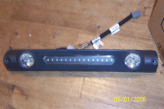Black third brake light bar with two round lamps and center LED strip, wiring pigtail on wood floor