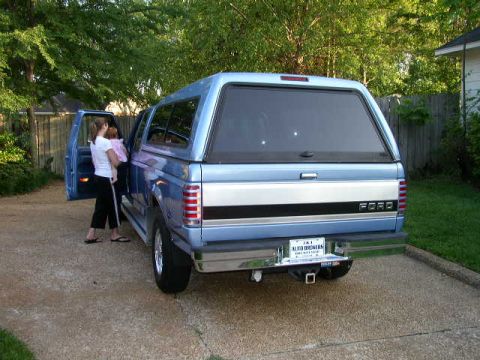 1995 Ford Bronco - Woman holding a baby near the open driver's door of a blue Ford pickup truck with a camper shell.