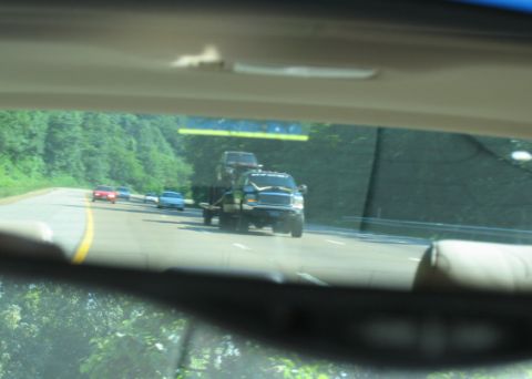 1988 Ford E250 - A pickup truck tows another vehicle on a highway, seen through a rearview mirror.