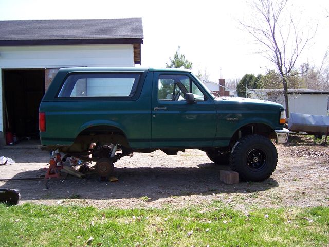 Green Ford Bronco on jack stands, rear wheel removed, front on black wheel with mud tire