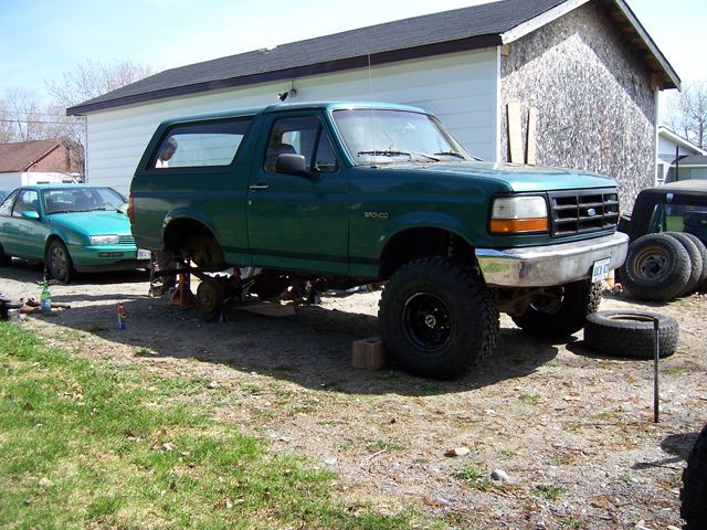 Green Ford Bronco on jack stands with rear wheel off, front on black wheel and mud tire