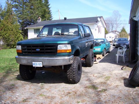 1996 Ford Bronco - A green Ford Bronco with a lifted suspension and oversized tires is parked in a driveway with other vehicles.