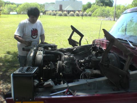 1991 Ford Bronco - A person works on the engine of a red vehicle with its hood open in a grassy yard.