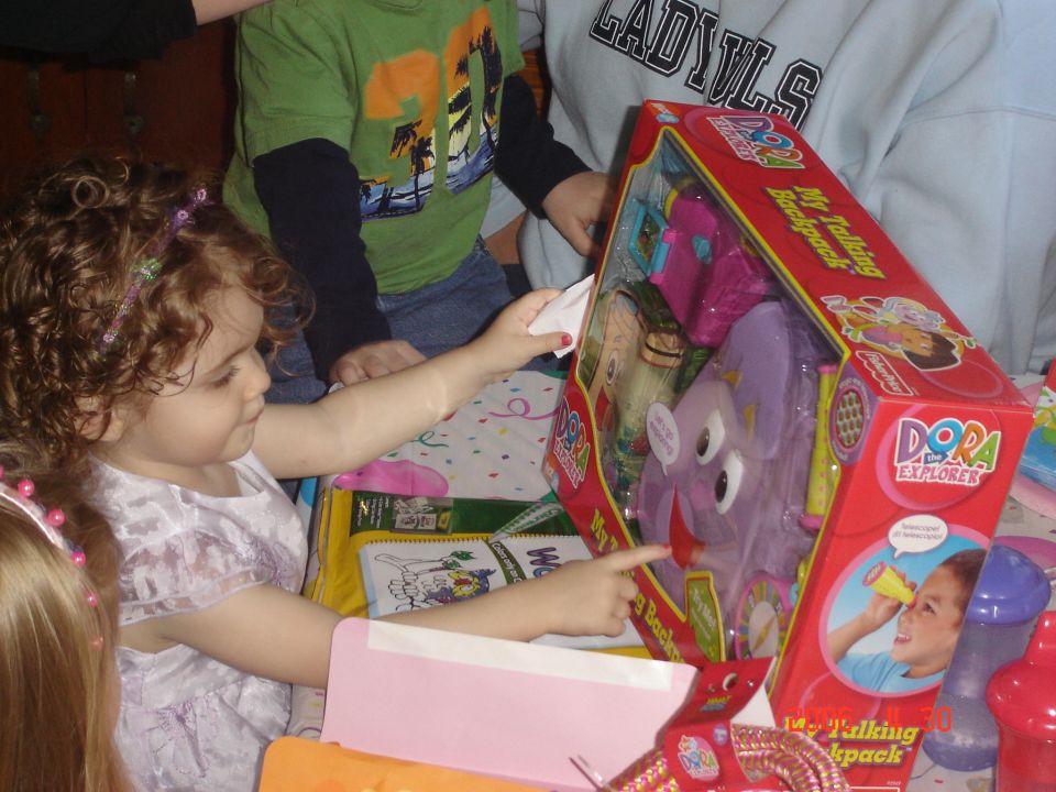 Children gathered around a table, opening a Dora the Explorer toy