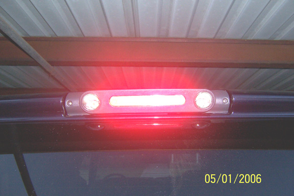 Lit red third brake light bar on dark blue vehicle rear window under metal shop roof