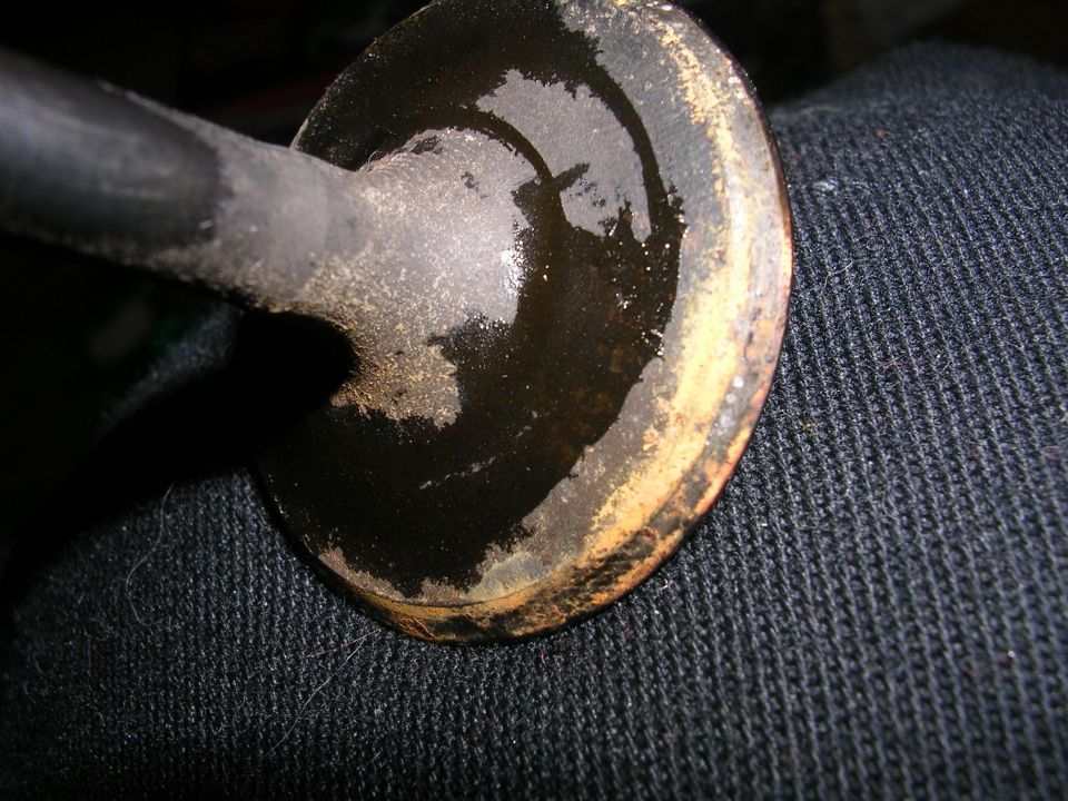 Engine valve with oil residue on its face and stem, resting on dark fabric