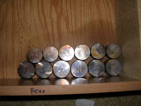 1996 Ford Probe - A collection of engine pistons are neatly arranged on a wooden shelf, with the word 'Rear' written on the shelf's edge.