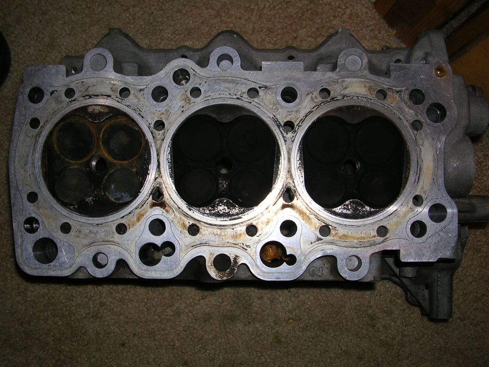 Engine cylinder head with three visible combustion chambers, showing carbon buildup and valve seats