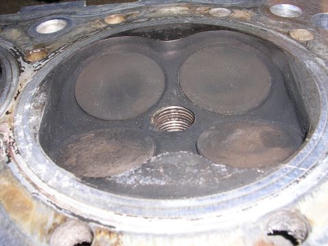 1996 Ford Probe - Close-up view of an engine cylinder head, showing four valves and a central threaded spark plug hole. Carbon deposits are visible on the va…