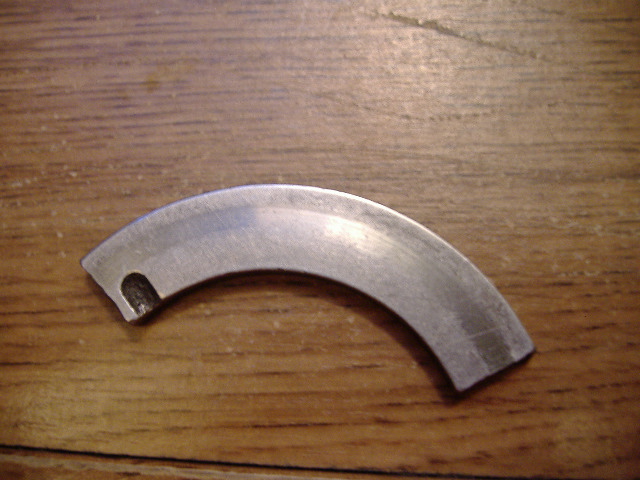 Curved metal engine bearing shell on a wooden surface