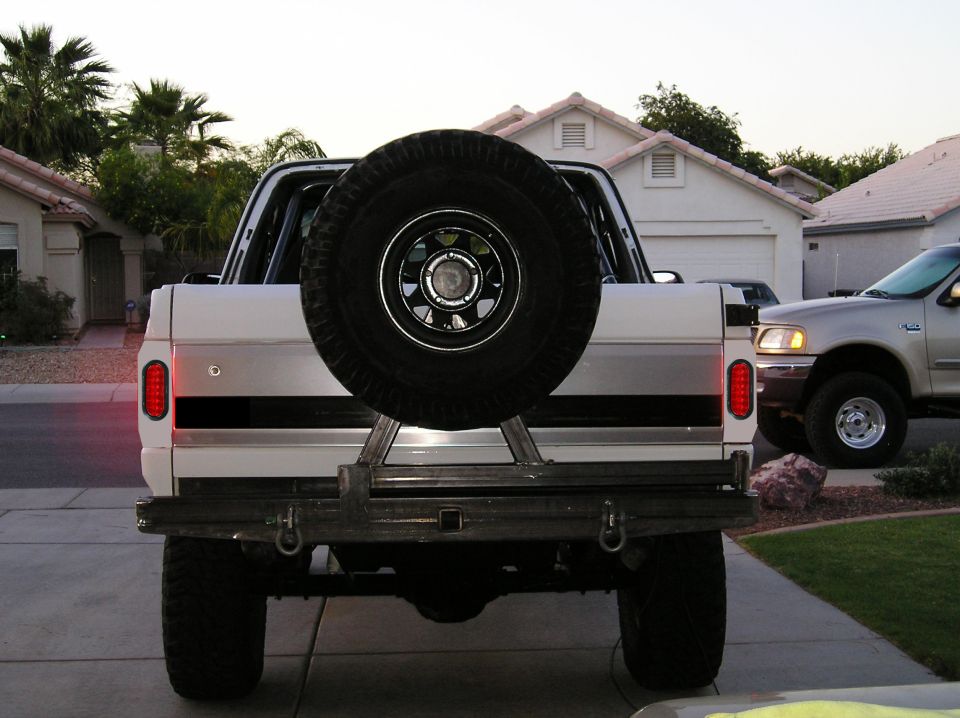 Rear of lifted white full-size SUV with swing-out spare tire and tube bumper