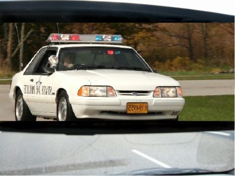 1993 Ford Mustang - A white police car with a light bar is seen from a slightly low angle.