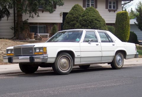 1972 Ford Ranchero - This white sedan, likely from the 1980s, is parked curbside in front of a house.
