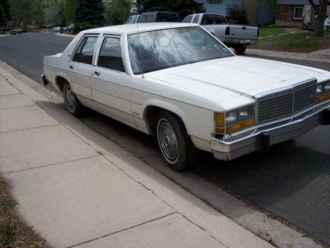 1972 Ford Ranchero - This white sedan, likely from the early 1980s, is parked on a suburban street next to a sidewalk. pickup truck.